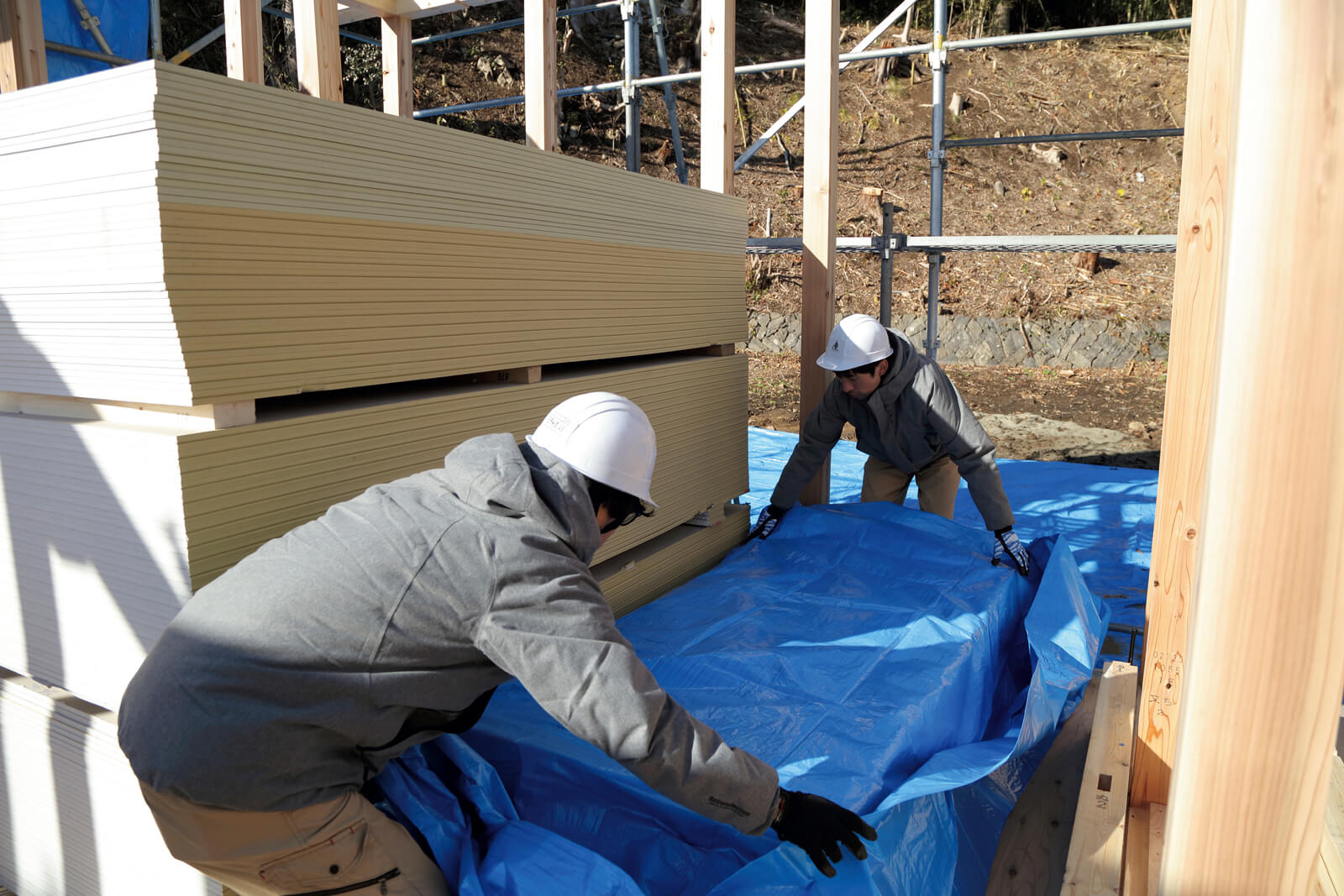 ヒノケンの工事現場では、敷地内に積まれた資材はもちろん、上棟作業完了後の柱や屋根などの材料が見えないようにすべてブルーシートで覆って養生している