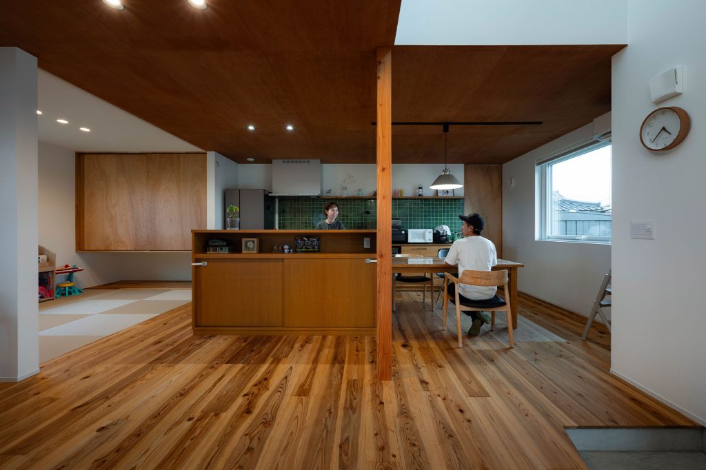 ダイニング・キッチンは、動線が機能的なアイランド型のストレートダイニング。キッチンのダークグリーンのアクセントウォールや木張り仕上げのLDKの天井が、空間に彩りとメリハリをもたらす