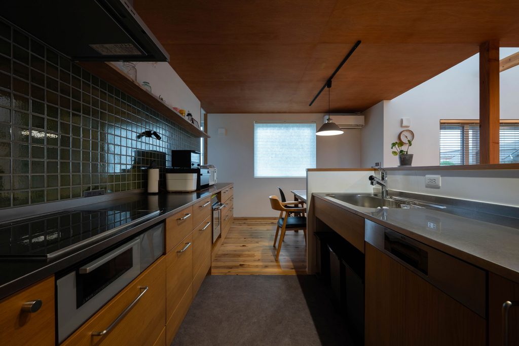 キッチンは対面側にシンク、背面収納側にIHクッキングヒーターを配したセパレート型。背面収納は既成のキッチンに面材などを組み合わせて造作した。「パンやお菓子をつくるのが趣味」という奥さんの希望でガスオーブンも導入